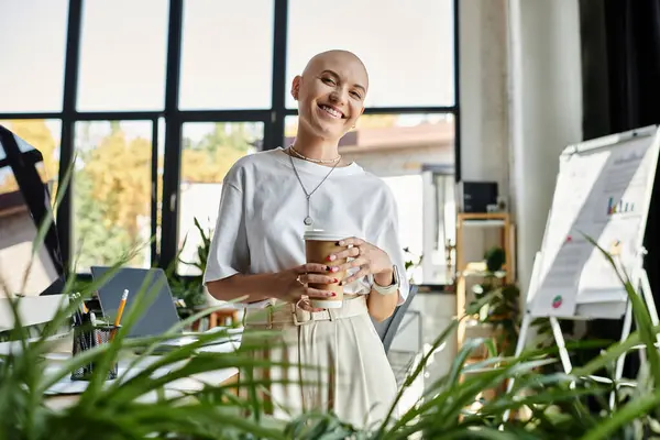 A joyful bald woman in elegant attire enjoys a warm drink surrounded by vibrant greenery. — Stock Photo