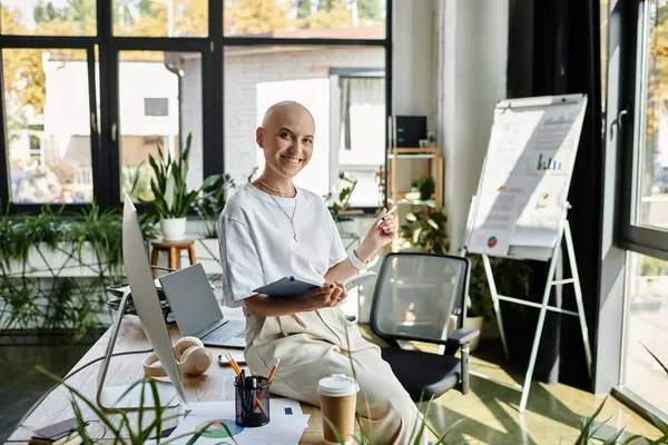 Une jeune femme chauve vêtue élégamment s'assoit dans un bureau vibrant, souriant joyeusement à la caméra. — Photo de stock