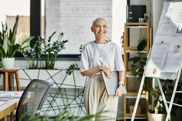 Sorride calorosamente mentre tiene in mano una tavoletta, circondata da un verde vibrante e un elegante spazio di lavoro. — Foto stock