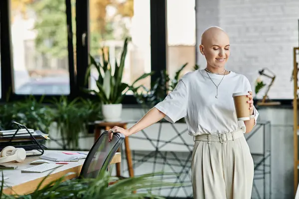 A young bald woman in elegant attire sips coffee, surrounded by lush plants and modern decor. — Stock Photo