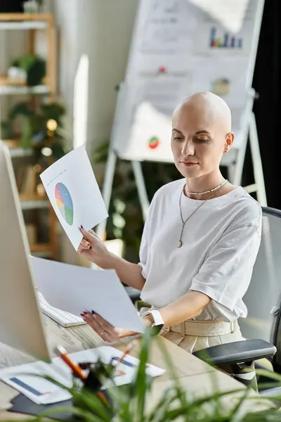 A young bald woman studies detailed reports and charts at her stylish workspace during the day. — Stock Photo