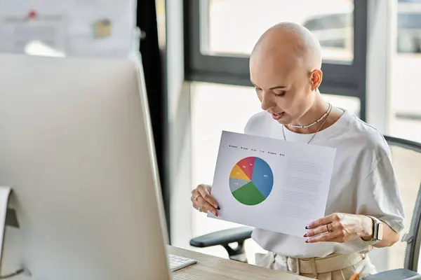 A young bald woman studies a vibrant report while seated at a desk in a modern office setting. — Stock Photo
