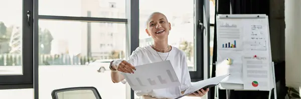 The young bald woman shares vibrant insights while standing in a well lit office space. — Stock Photo