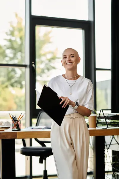 A young bald woman stands confidently, holding documents in a stylish office environment. — Stock Photo