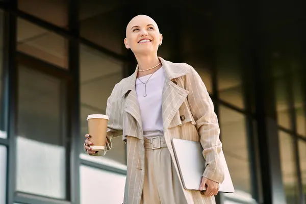 A stylish bald woman holds a coffee cup and laptop, radiating confidence on her day out. — Stock Photo