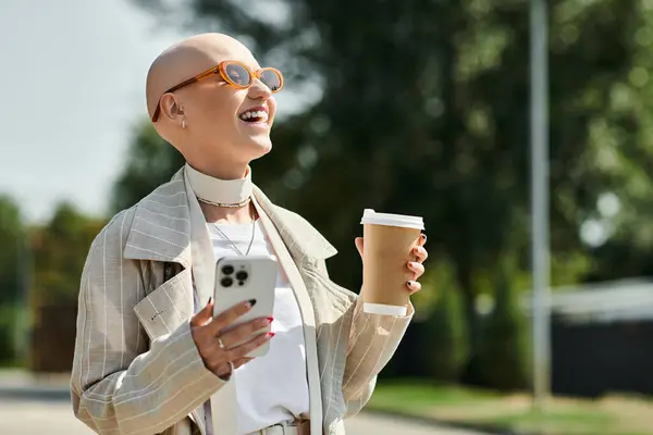 The young woman smiles widely while holding a smartphone and coffee cup, exuding joy. — Stock Photo