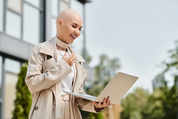 A young bald woman dressed elegantly smiles while engaging with her laptop outside. — Stock Photo