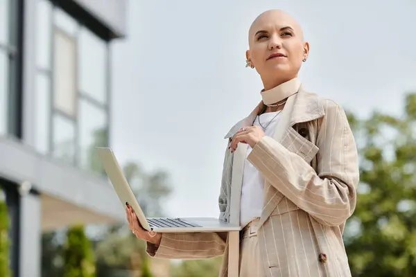 A confident young bald woman, dressed elegantly, engages with her laptop outside amid greenery. — Stock Photo