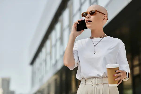A young bald woman sips coffee and chats on her phone in a stylish outdoor setting. — Stock Photo