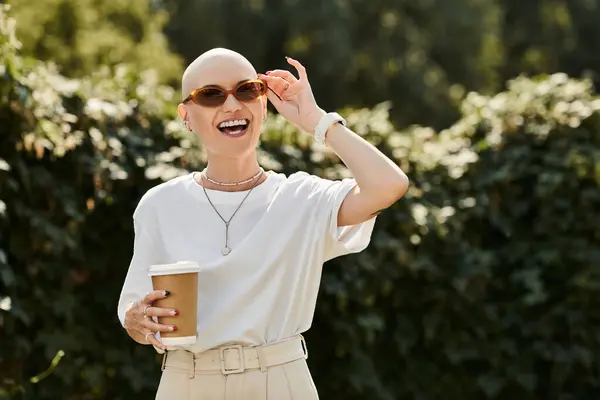 A young bald woman beams with joy while sipping coffee in elegant attire under the sun. — Stock Photo