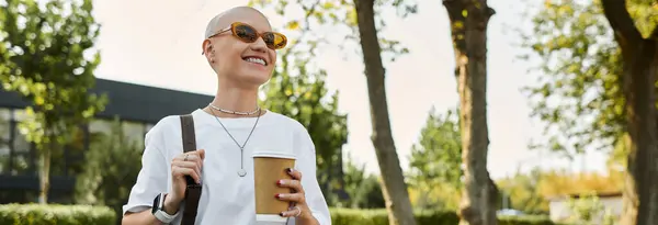 The woman smiles brightly while holding a coffee cup, dressed elegantly amidst greenery. — Stock Photo