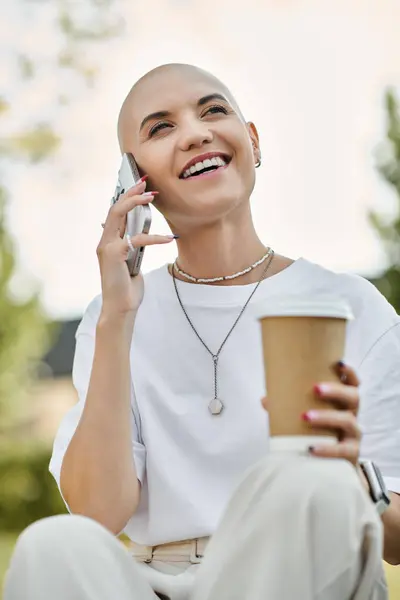 Smiling brightly, a young bald woman engages in a cheerful phone conversation while sipping coffee. — Stock Photo