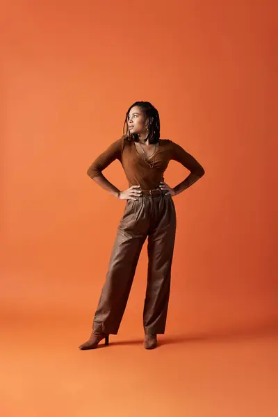 Una giovane donna afroamericana alla moda mette in mostra il suo stile con i capelli intrecciati in uno studio vibrante. — Foto stock