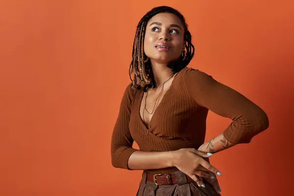 Una joven afroamericana con cabello trenzado muestra su estilo y confianza en un estudio creativo. - foto de stock