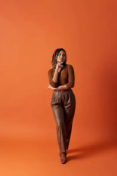 A young woman with braided hair stands elegantly in a studio with a striking orange backdrop. — Stock Photo