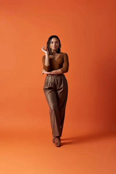 A young and stylish woman showcases her braided hair in a warm-toned studio, exuding confidence and poise. — Stock Photo