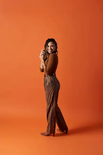 A young, fashionable African American woman poses confidently in a studio with a warm orange background. — Stock Photo