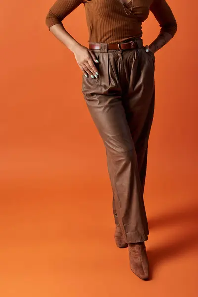 Una mujer joven y vanguardista exhibe su elegante atuendo contra un llamativo fondo naranja. - foto de stock