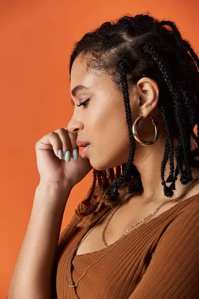 A young, stylish woman with braids poses thoughtfully in a vibrant studio atmosphere, showcasing her elegance. — Stock Photo