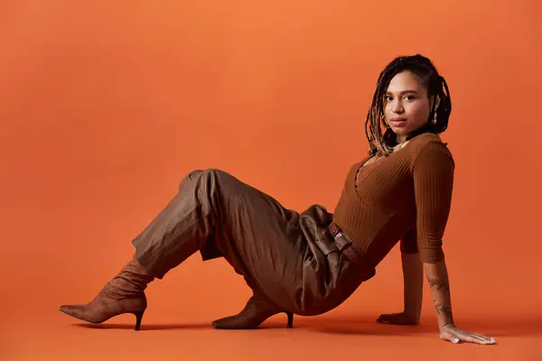A fashionable young woman with braided hair sits elegantly against a bright background, exuding confidence. — Stock Photo