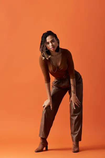 A stylish African American woman poses confidently against a warm orange backdrop, highlighting her unique style. — Stock Photo