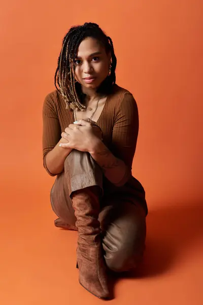 A fashionable young African American woman with braided hair elegantly poses against a vibrant orange backdrop. — Stock Photo