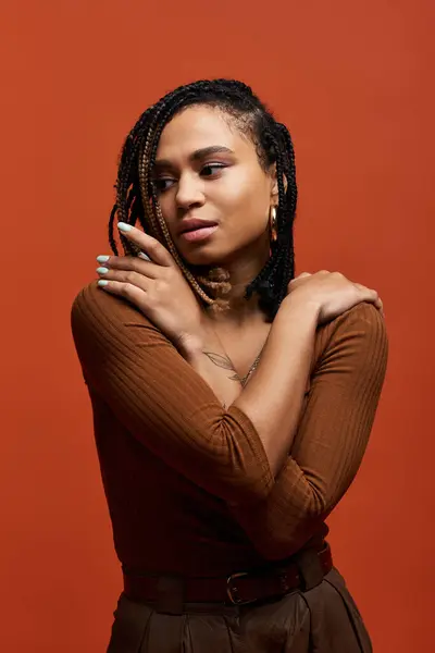 A young African American woman with braided hair elegantly poses in a warm-toned studio, radiating confidence. — Stock Photo