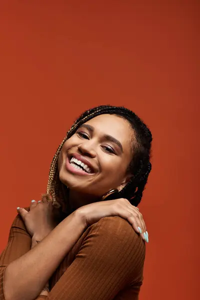A young and fashionable African American woman beams with joy, showcasing her braided hair in a studio backdrop. — Stock Photo
