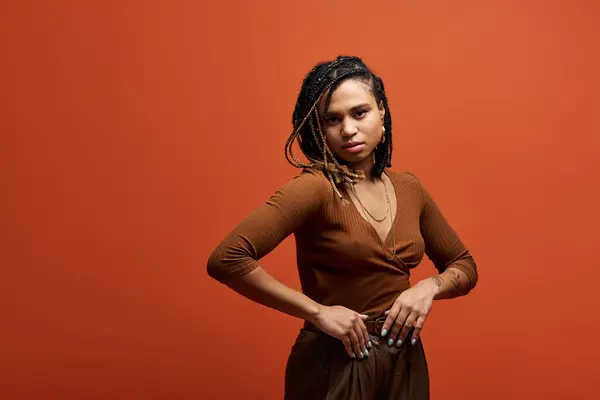 A young African American woman exudes confidence while posing in a vibrant studio setting with braided hair. — Stock Photo