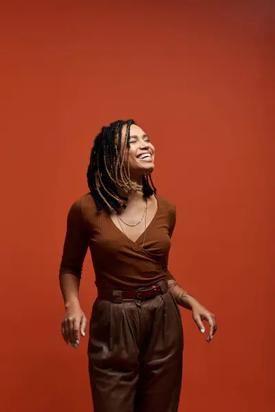 A vibrant young woman with braided hair expresses joy while posing against a rich red background. — Stock Photo