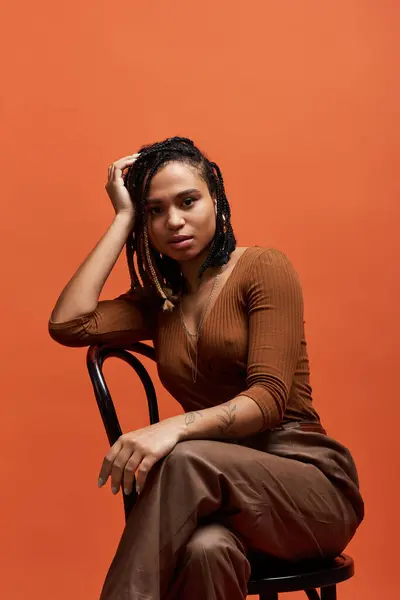 A young African American woman with braided hair showcases her style while posing against an orange backdrop. — Stock Photo