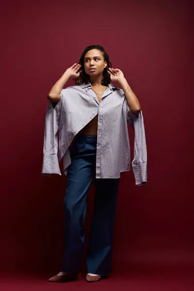 A young African American woman with braids poses stylishly in a studio, showcasing her trendy outfit and confidence. — Stock Photo