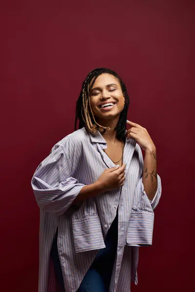 Una giovane donna afroamericana con i capelli intrecciati gode di un momento gioioso in uno studio vibrante, mostrando il suo stile. — Foto stock