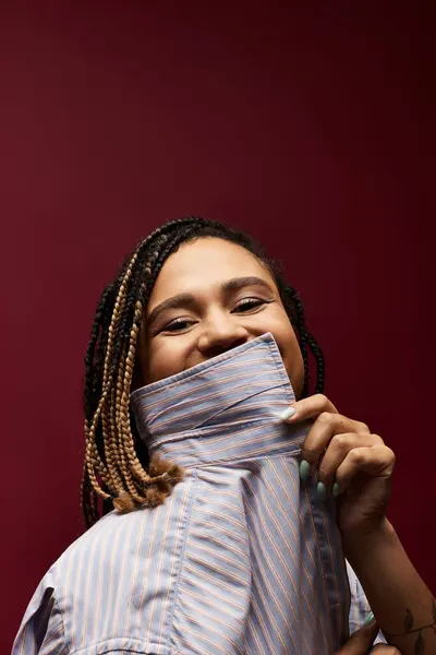A young African American woman playfully hides her smile behind an oversized collar in a studio space. — Stock Photo
