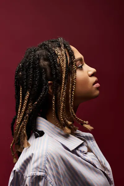 A young woman showcases her unique braided hairstyle against a rich backdrop, exuding confidence and style. — Stock Photo
