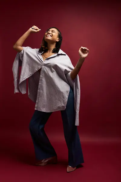 A joyful, young woman with braided hair dances in a studio, showcasing her vibrant energy and fashion sense. — Stock Photo