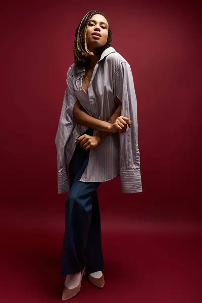 A young African American woman showcases her style with braided hair and a chic outfit in a vibrant studio backdrop. — Stock Photo