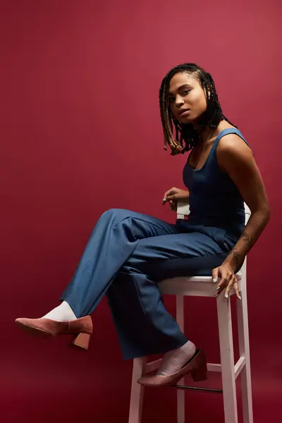 Une jeune afro-américaine aux cheveux tressés respire la confiance tout en posant dans un cadre de studio vibrant. — Photo de stock