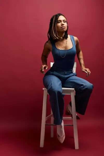 A stylish young woman with braided hair sits gracefully on a stool, radiating confidence in a vibrant studio. — Stock Photo