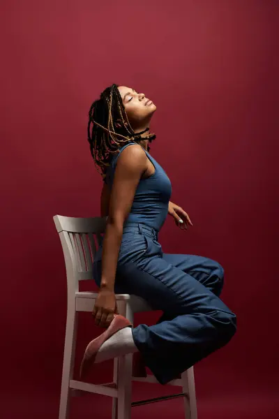 A young African American woman with braided hair poses elegantly in a vibrant studio, showcasing her style. — Stock Photo