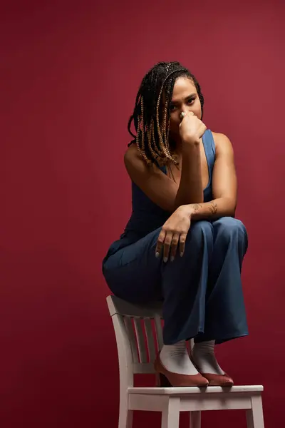 A young African American woman with braided hair poses on a chair, showcasing a stylish and contemplative mood. — Stock Photo