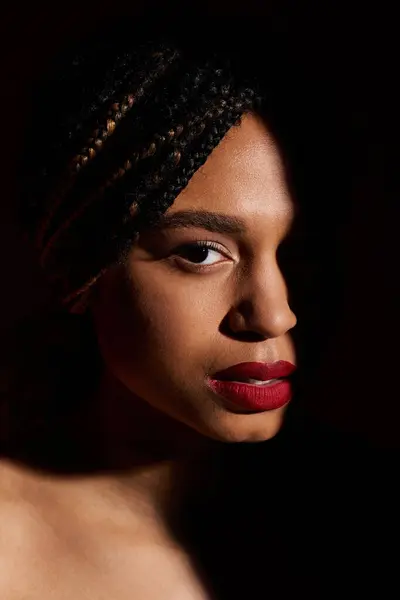 Una joven afroamericana exhibe su cabello trenzado y sus labios rojos en un ambiente creativo de estudio. - foto de stock
