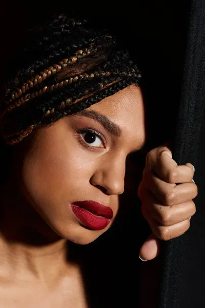 A stylish young woman with intricate braids and bold red lips poses confidently in a chic studio setting. — Stock Photo