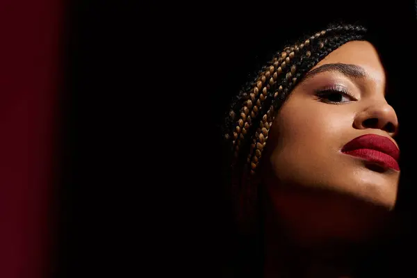 A confident young woman showcases her braided hairstyle and bold red lips in a striking studio setting. — Stock Photo
