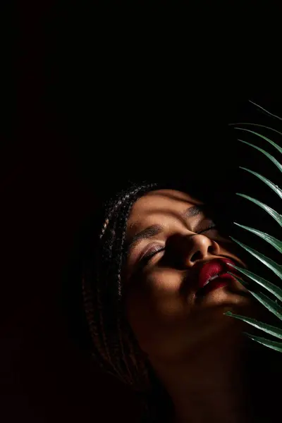 Une jeune femme aux cheveux tressés affiche des lèvres rouges vibrantes tout en posant gracieusement dans un studio. — Photo de stock