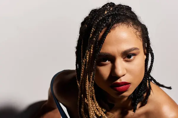 A young African American woman with striking braids and red lips strikes a bold pose in a sleek studio. — Stock Photo