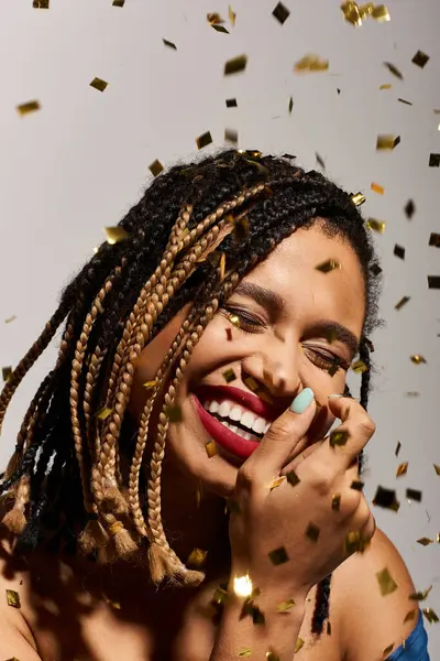 A young and fashionable African American woman with braided hair beams with joy, surrounded by golden confetti. — Stock Photo