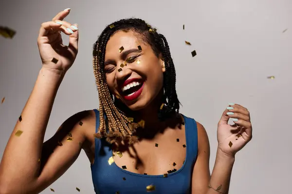 The stylish African American woman with braided hair radiates joy while celebrating in a lively studio. — Stock Photo