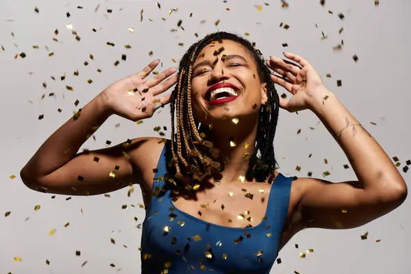 A young, fashionable woman with braided hair and red lips celebrates joyfully in a studio filled with confetti. — Stock Photo