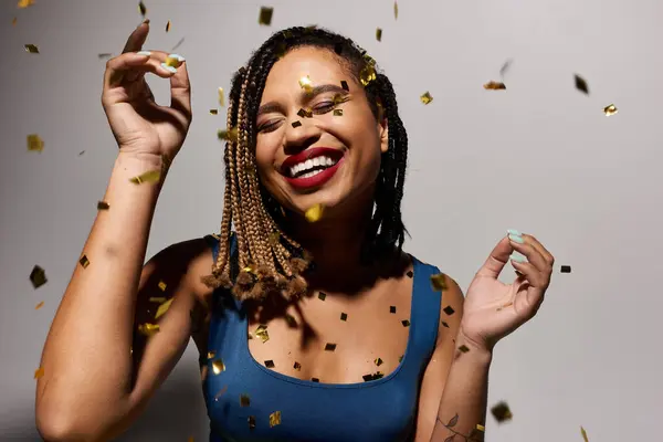 A young woman with braided hair and red lips joyfully poses in a studio, surrounded by vibrant confetti. — Stock Photo